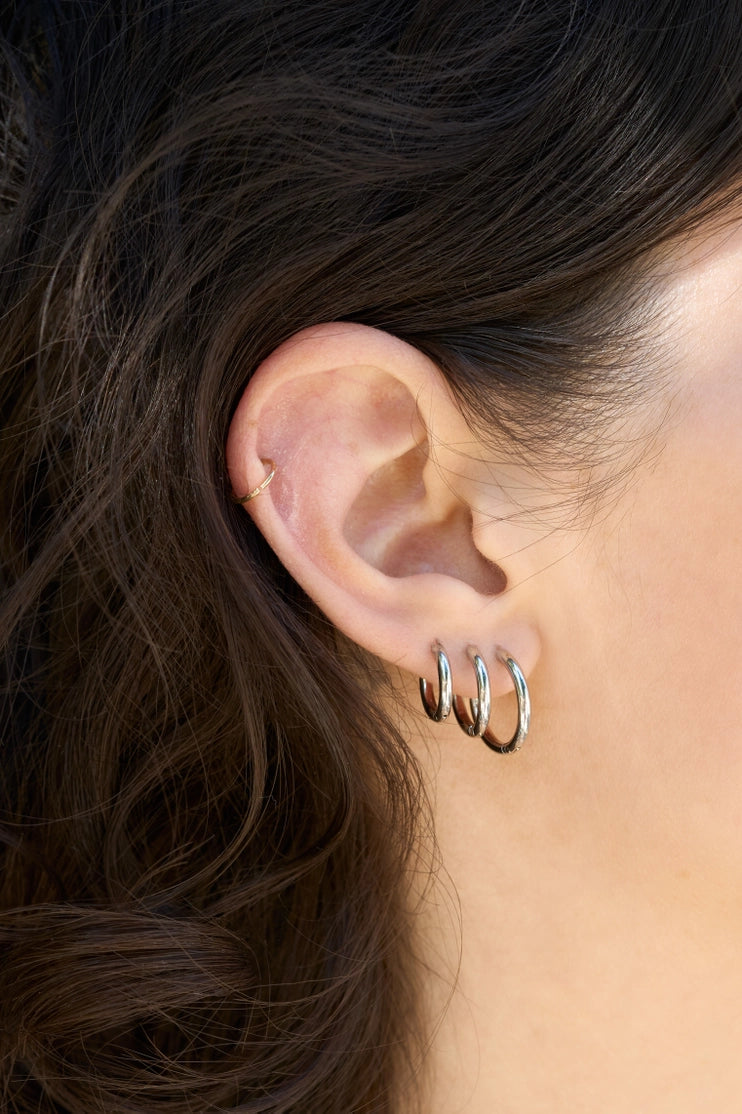 Trío de aros huggie plateados apilados en oreja