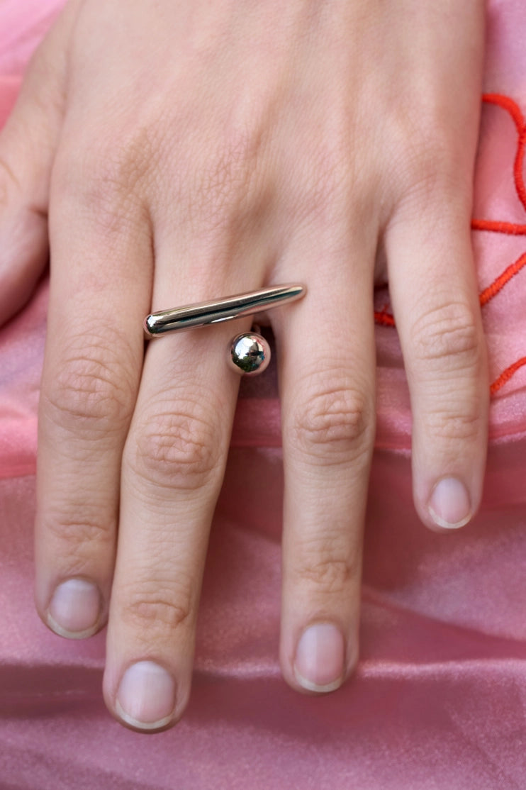 Anillo de equilibrio en tono plateado sobre fondo rosa