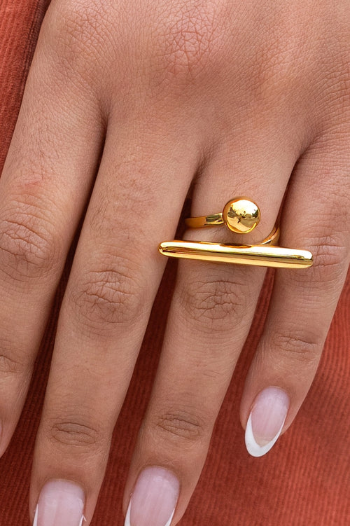 Anillo de equilibrio chapado en oro 18K con barra y esfera dorada en mano
